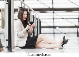 Mature business woman sitting down during a break and texting on her smart phone; Edmonton, Alberta, Canada