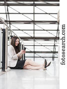 Mature business woman sitting down during a break and texting on her smart phone; Edmonton, Alberta, Canada