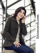 Mature business woman talking on her cell phone while taking a break in the atrium of an office building; Edmonton, Alberta, Canada