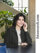 Mature business woman talking on her cell phone while taking a break in the atrium of an office building; Edmonton, Alberta, Canada