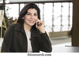 Mature business woman talking on her cell phone while taking a break in the atrium of an office building; Edmonton, Alberta, Canada