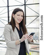 Mature business woman texting in the atrium of an office building; Edmonton, Alberta, Canada