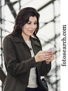 Mature business woman texting while taking a break in the atrium of an office building; Edmonton, Alberta, Canada