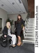Portrait of two professional business women in the lobby of an office, one of which is a paraplegic in a wheelchair; St. Albert, Alberta, Canada