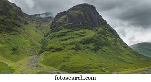 Storm clouds over rugged and foliage covered mountains; Scotland
