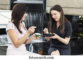 Two business women having lunch together in the atrium of an office building; Edmonton, Alberta, Canada