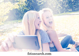 Two sisters having fun outdoors in a city park in autumn and laughing at the selfies they have taken of themselves; Edmonton, Alberta, Canada