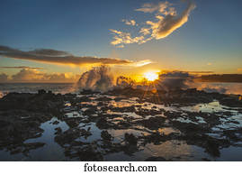 Waves crash over a rock outcrop at sunrise; Kauai, Hawaii, United States of America