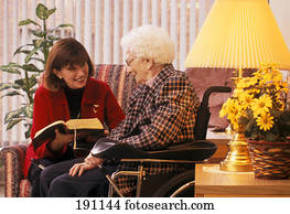 Woman reading to senior relative on wheelchair Woman reading to senior relative on wheelchair