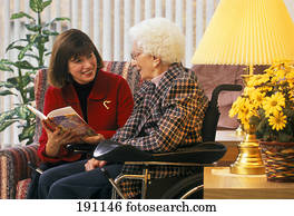 Woman reading to senior relative in wheelchair Woman reading to senior relative in wheelchair