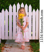 Girl with yellow flowers in front of picket fence