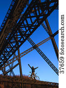 Cyclist under steel trestle bridge
