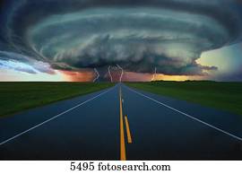 Single lane road leading to thundercloud