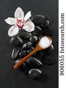 A spoon of mineral salt and an orchid lying on top of hot stone therapy stones