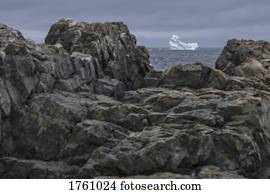 View of iceberg in sea through rocks on shore, Fogo Island, Newfoundland, Canada
