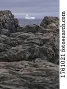 View of iceberg in sea through rocks on shore, Fogo Island, Newfoundland, Canada