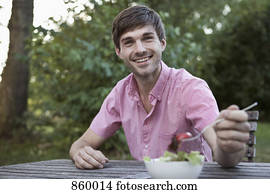 A man eating at a table outdoors, non-urban scene