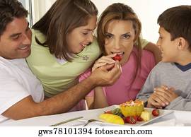 Mid adult man feeding a mid adult woman a strawberry with their two children beside them