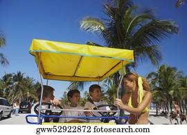 Three boys sitting on a buggy with a young woman standing beside them