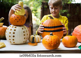 Girl and brother stacking carved pumpkins on garden table