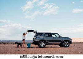 Young woman in remote setting, opening boot of SUV, dog beside her, Mexican Hat, Utah, USA
