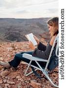 Young woman in remote setting, sitting on camping chair, reading book, Mexican Hat, Utah, USA