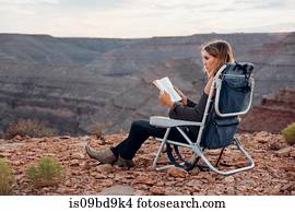 Young woman in remote setting, sitting on camping chair, reading book, Mexican Hat, Utah, USA