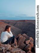 Young woman in remote setting, sitting on rocks, looking at view, Mexican Hat, Utah, USA