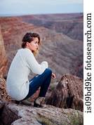 Young woman in remote setting, sitting on rocks, looking at view, Mexican Hat, Utah, USA