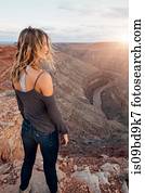 Young woman in remote setting, standing on cliff edge, looking at view, rear view, Mexican Hat, Utah, USA