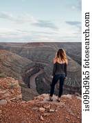 Young woman in remote setting, standing on cliff edge, looking at view, rear view, Mexican Hat, Utah, USA