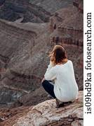 Young woman in remote setting, crouching on rocks, looking at view, rear view, Mexican Hat, Utah, USA