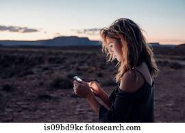 Young woman in remote setting, using smartphone, Mexican Hat, Utah, USA