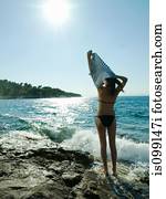 Young woman taking off t-shirt by the sea