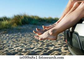 Mid adult couple sitting barefoot on car on beach