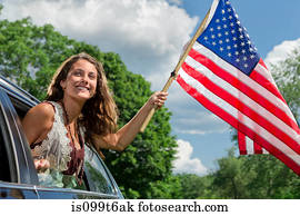 Teenage girl leaning out of car window holding american flag