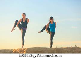 Two women practising yoga on top of a rock