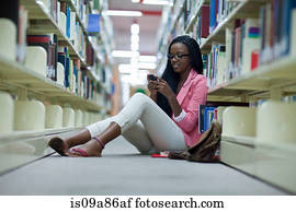 Female student sitting on floor in library using smartphone