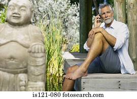 Man beside pool and buddha with cellphone