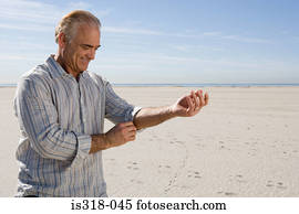 Senior man rolling up sleeve on beach