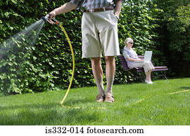 Man watering lawn and woman using laptop