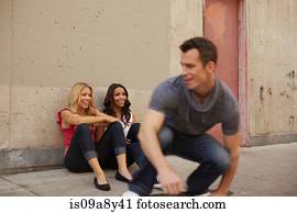Man skating past women sitting on ground