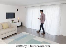 Man with mobile phone walking past curtains