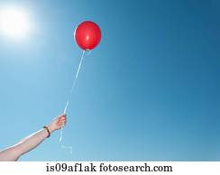 Hand holding single red balloon against blue sky