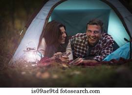Mature couple lying together in tent, playing card game