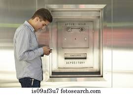 Mid adult man banking on cellphone next to bank deposit box