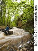 Male hiker sitting on flooded river rock, Naramata, British Columbia, Canada