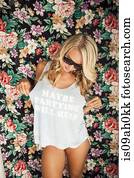 Young woman wearing slogan vest in front of floral wallpaper