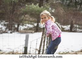 Young girl climbing wire fence in field