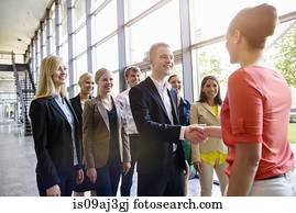 Team of business men and women greeting client in office